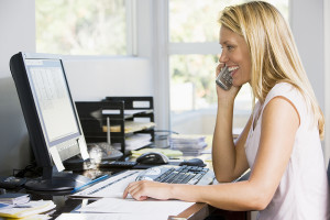 Woman in home office with computer using telephone smiling